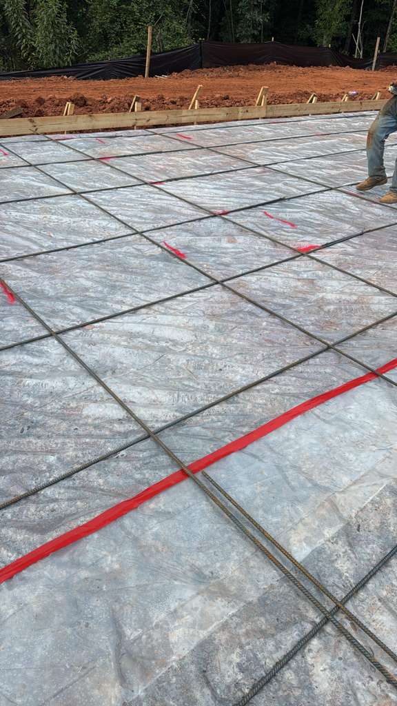 Rebar grid tied over vapor barrier with marked layout lines before a slab pour